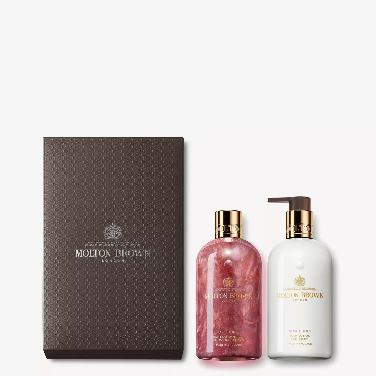 The Rose Dunes Body Care Gift Set by Molton Brown Cyprus includes a patchouli Sulawesi-infused pink body wash with a gold cap and a white lotion with a pump. Both are elegantly packaged in a dark brown box featuring the Molton Brown logo.