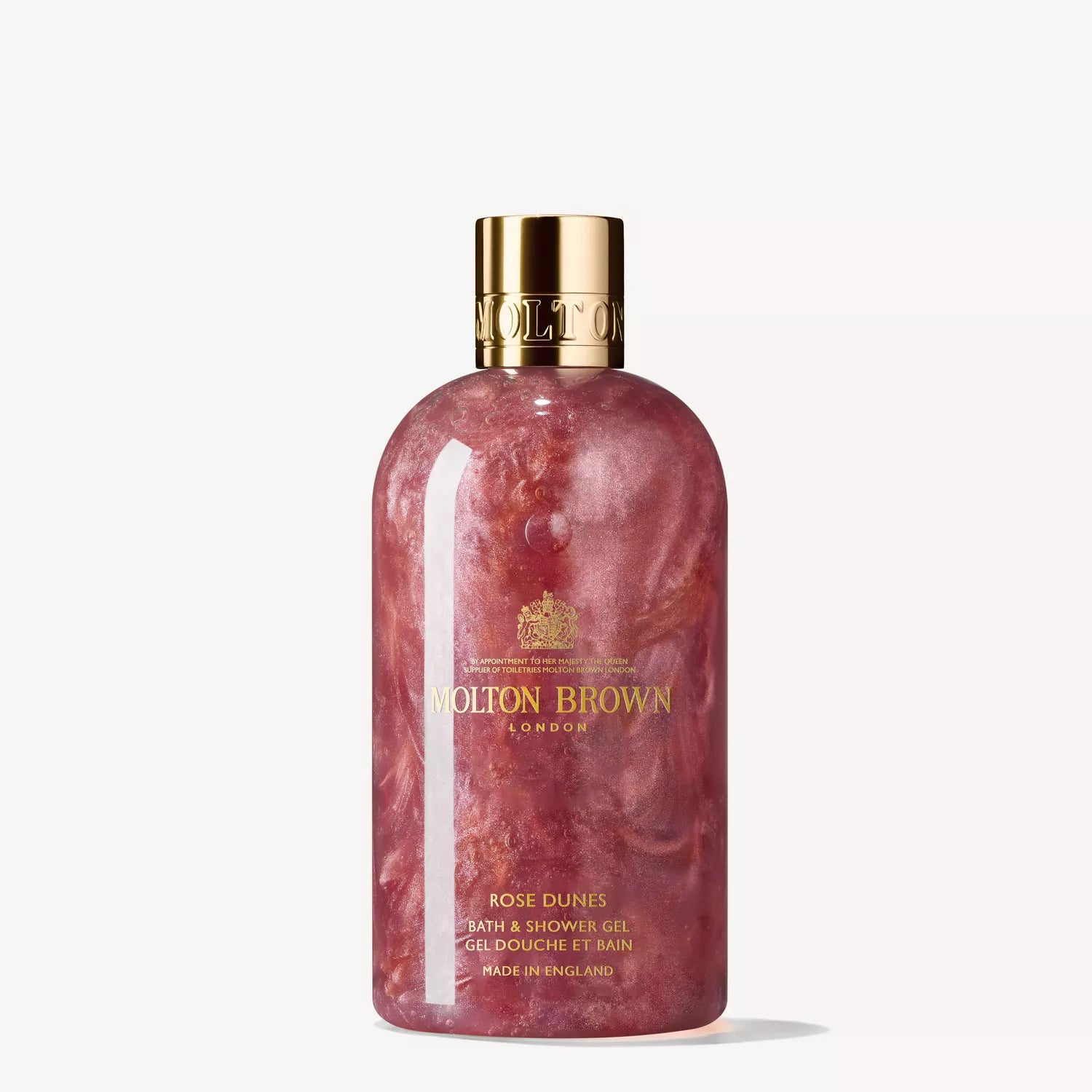 A Molton Brown Cyprus Rose Dunes Body Care Gift Set includes a transparent bottle of bath and shower gel with hints of patchouli Sulawesi, shimmering pink gel inside, adorned with gold accents and text.