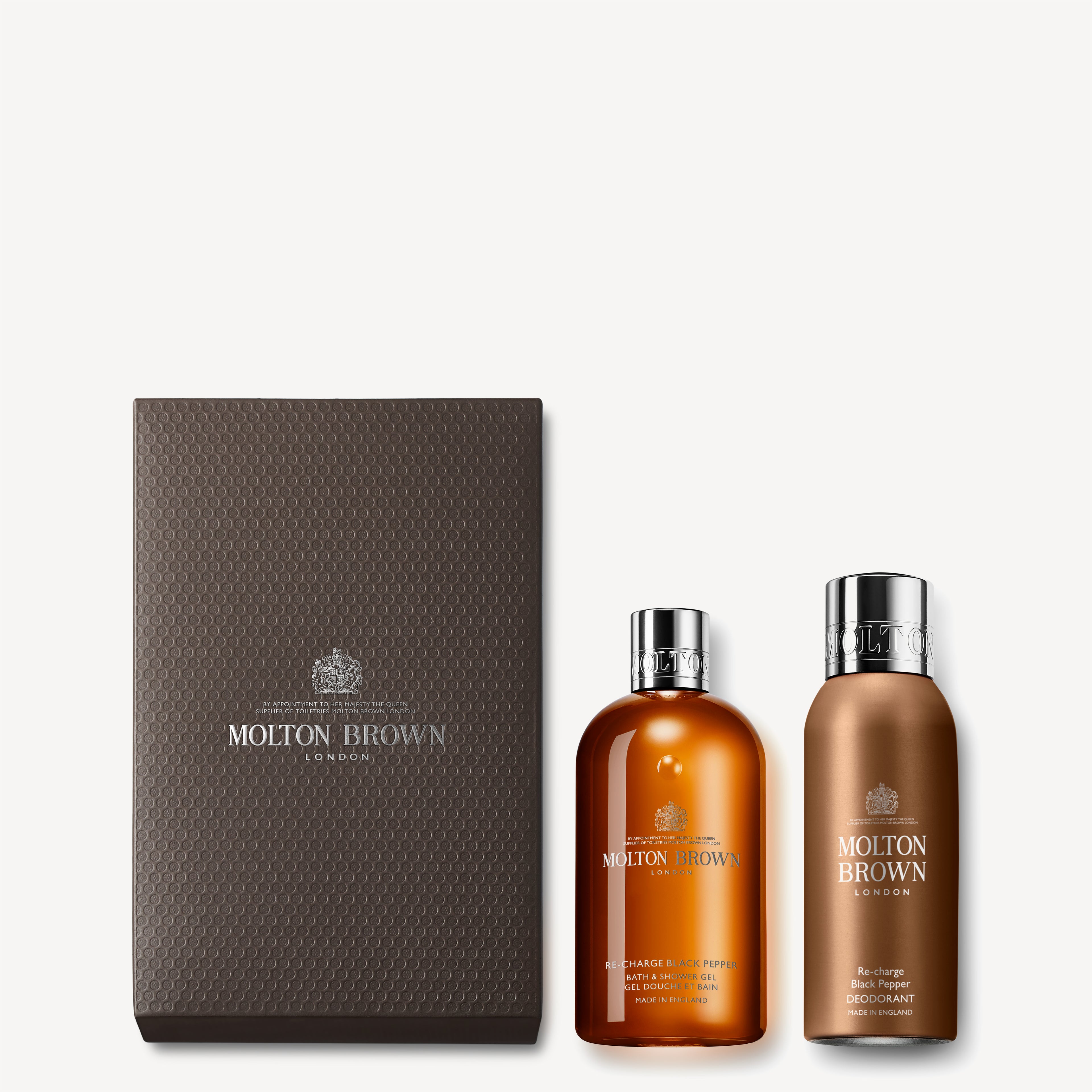 The Fresh Re-charge Black Pepper Gift Set from MoltonBrown Cyprus comes in a dark textured box and features two bottles: one is transparent brown, infused with invigorating black pepper body wash, and the other is a metallic bronze deodorant. Both products are adorned with silver caps and the Molton Brown branding, adding a touch of luxury and sophistication.