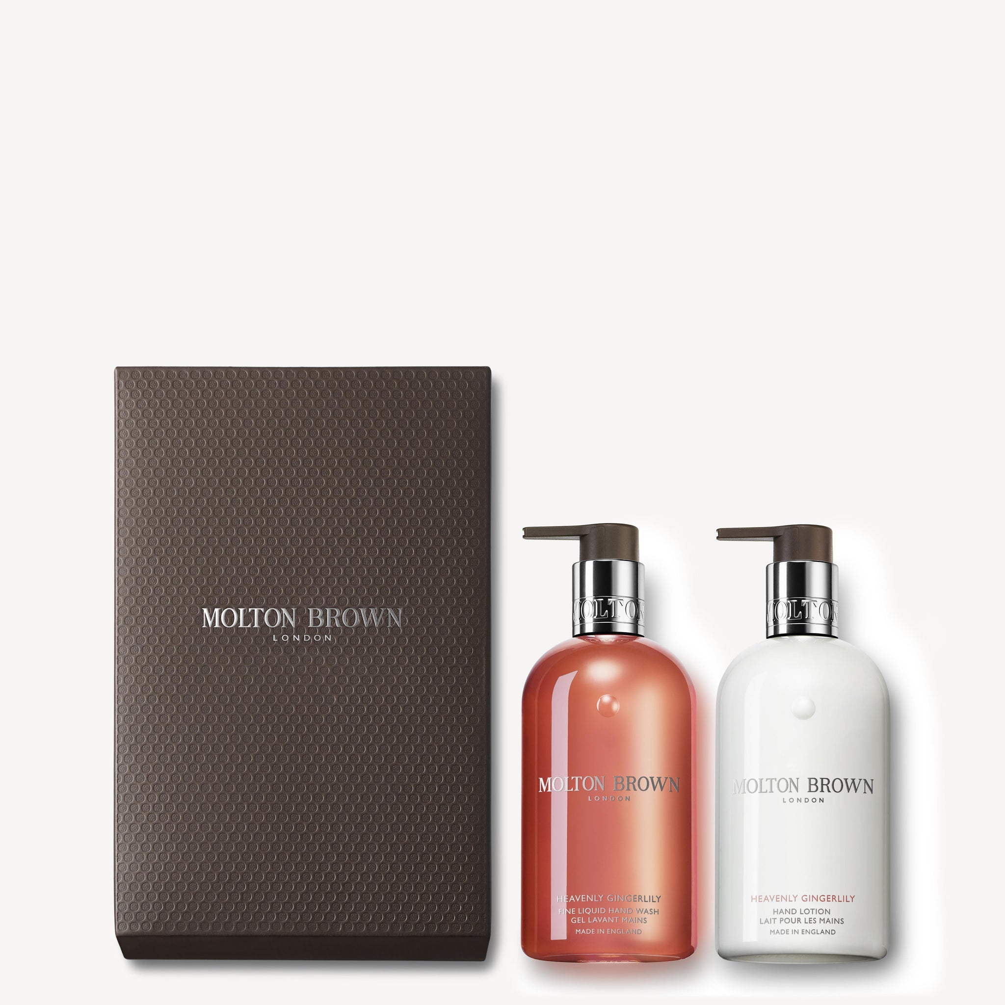 A sophisticated display showcases the MoltonBrown Cyprus Heavenly Gingerlily Hand Wash & Lotion Set, featuring a brown textured box and two pump bottles—one pink and one white. The set includes both a luxurious Hand Lotion and Liquid Hand Wash, while the serene background maintains a light, calming color.