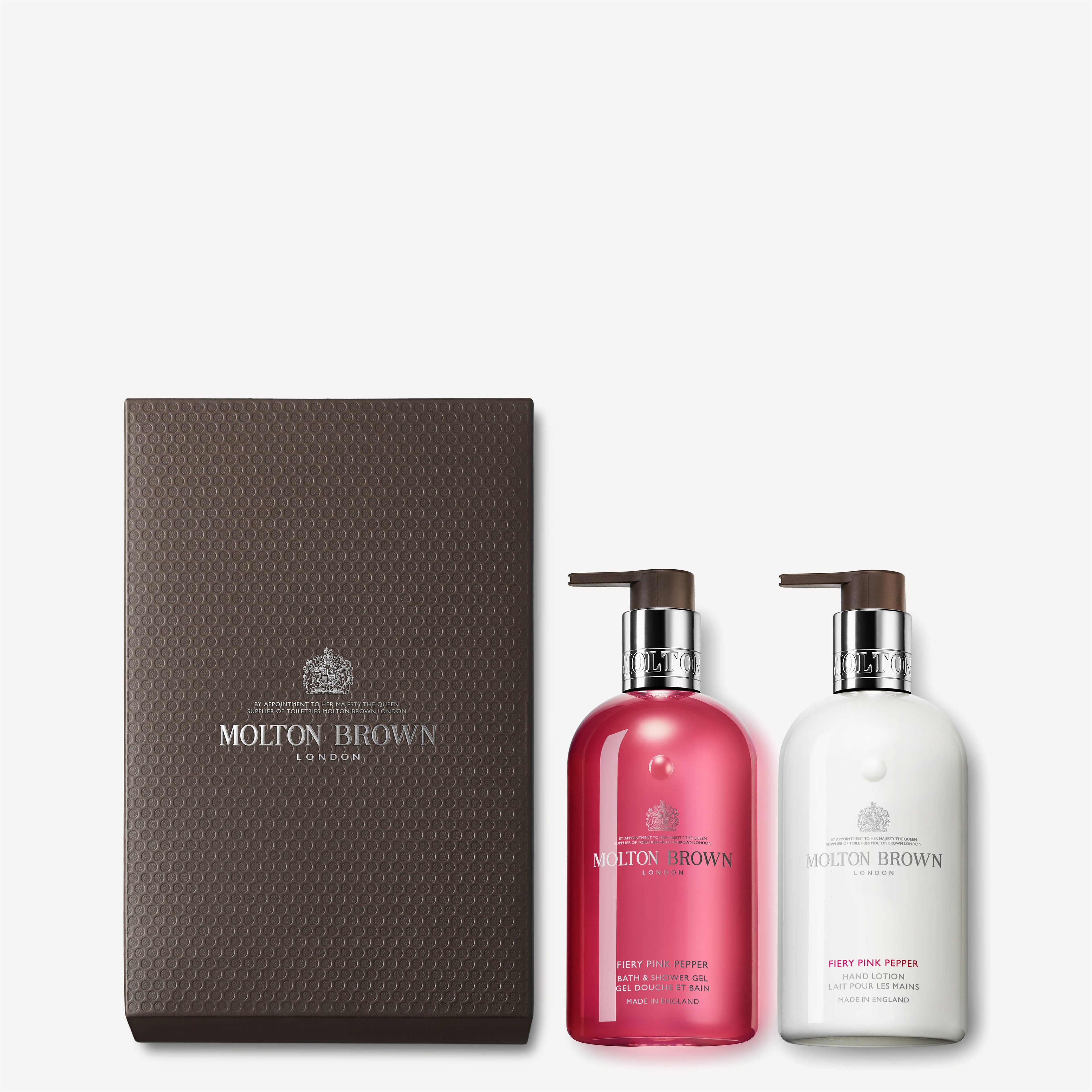 The MoltonBrown Cyprus Fiery Pink Pepper Hand Wash & Lotion Set comes in a textured brown box containing two pump bottles. Infused with invigorating pink pepper and ginger, the set includes a pink-labeled Fiery Pink Pepper Bath & Shower Gel and a white-labeled Fiery Pink Pepper Body Lotion, offering a revitalizing experience.