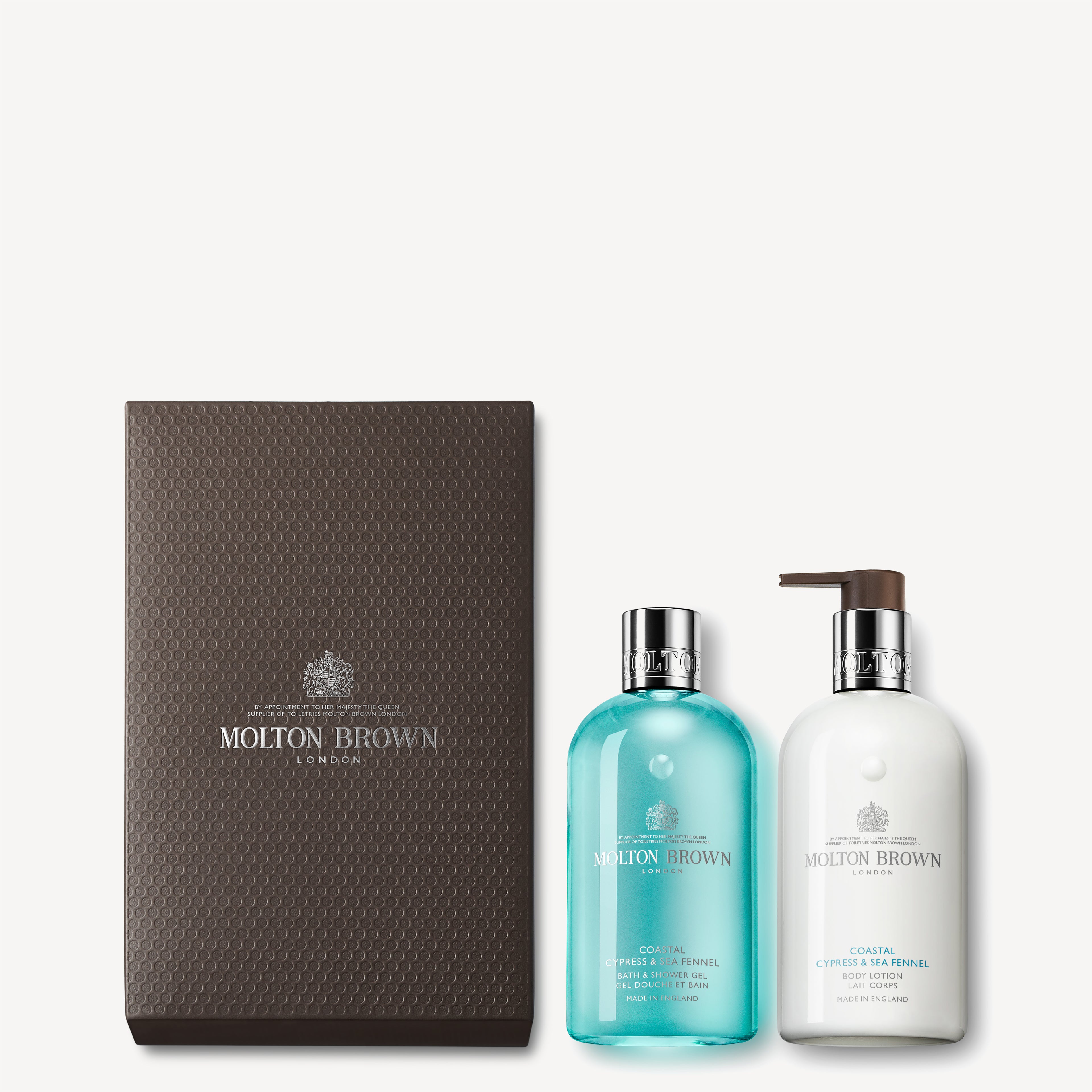 The MoltonBrown Cyprus Coastal Cypress & Sea Fennel Shower Gel & Lotion Set comes in a textured brown box and features a Bath & Shower Gel with a transparent bottle, blue liquid, and silver cap, alongside a Body Lotion with a white pump dispenser.