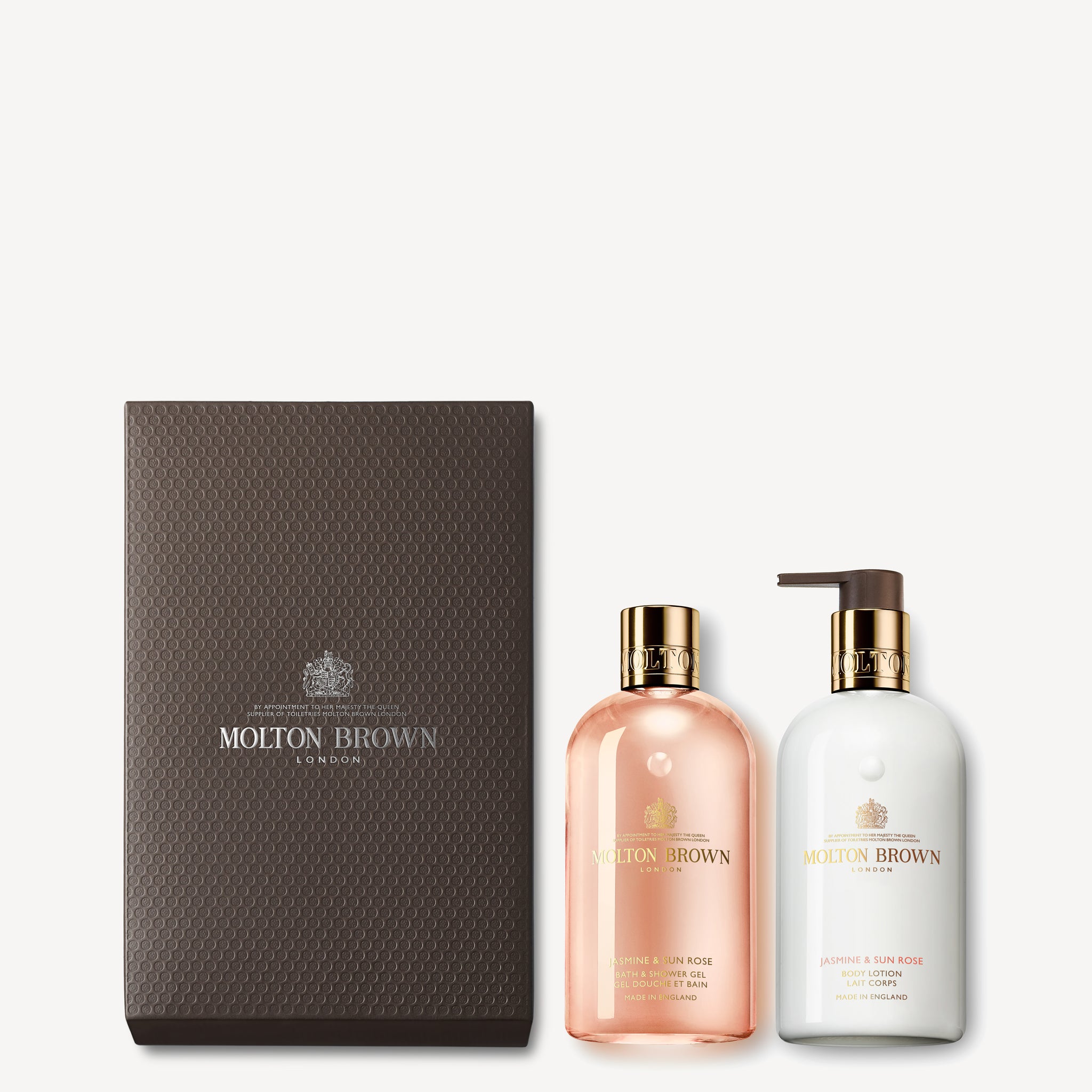 The MoltonBrown Cyprus Jasmine & Sun Rose Shower Gel & Lotion Gift Set comes in a dark textured box. It includes a clear bottle with pink liquid, and an opaque bottle with white cream, both finished with gold and brown lids.