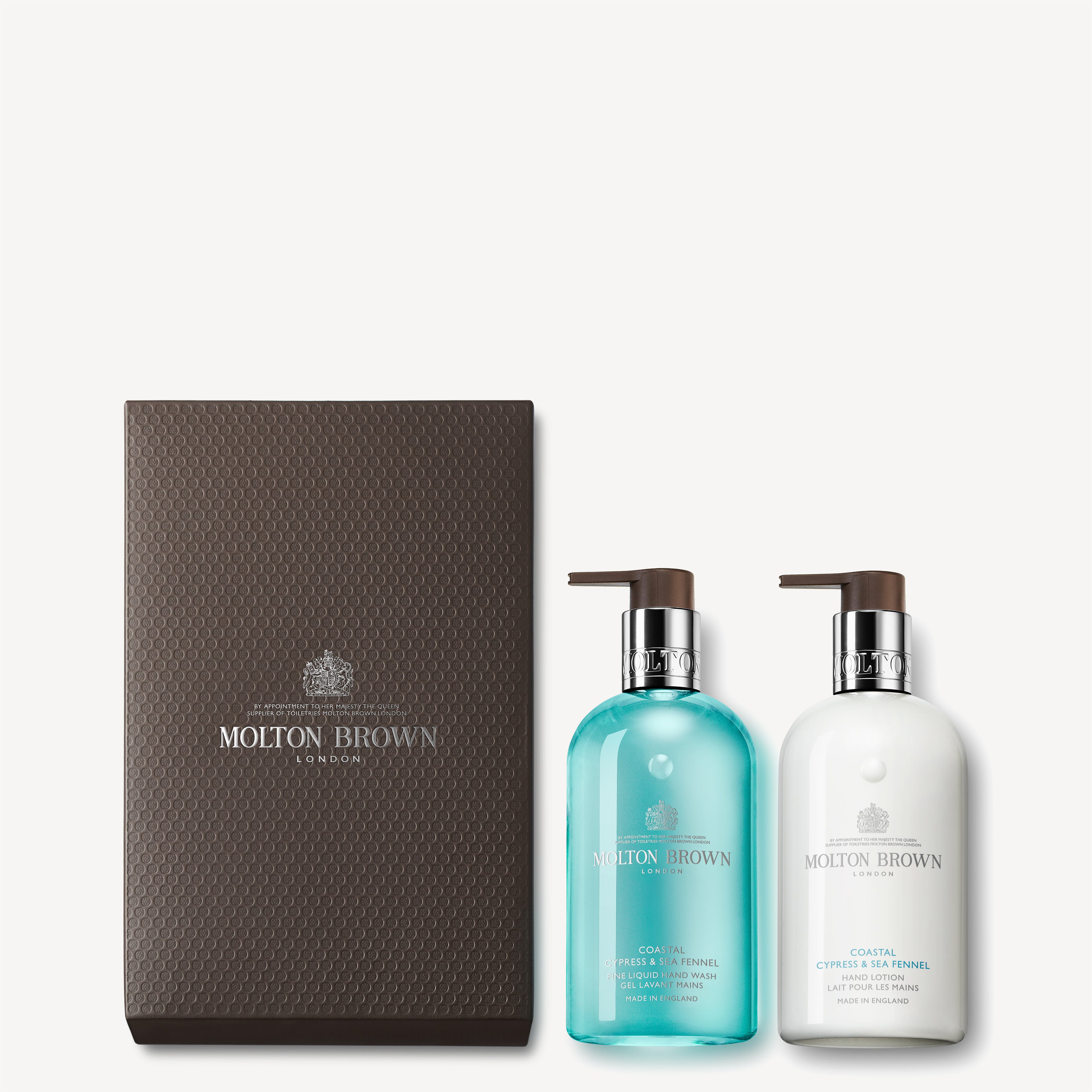 This Coastal Cypress & Sea Fennel Hand Wash & Lotion Set by MoltonBrown Cyprus is elegantly presented in a textured dark brown box. It includes two pump bottles: one blue and one white, offering a luxurious Fine Liquid Hand Wash and Hand Lotion for an indulgent sensory experience.